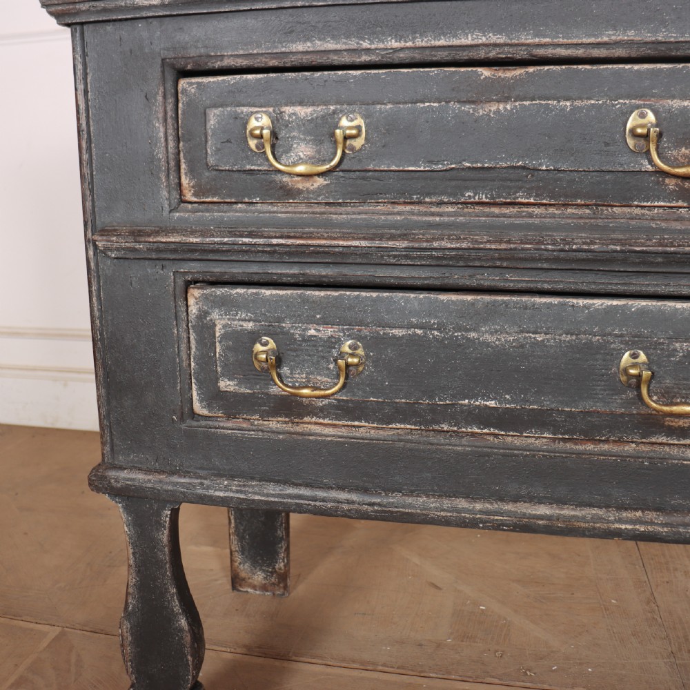 An English painted dresser base featuring a dark charcoal finish, four wide drawers with brass drop handles, shaped corner legs, and a light marble top. View VI