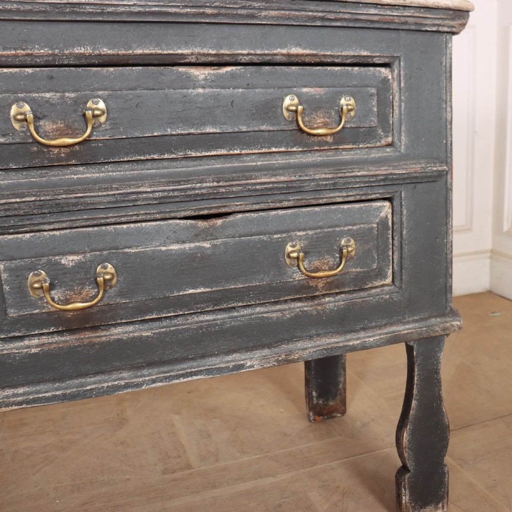 An English painted dresser base featuring a dark charcoal finish, four wide drawers with brass drop handles, shaped corner legs, and a light marble top. View VII