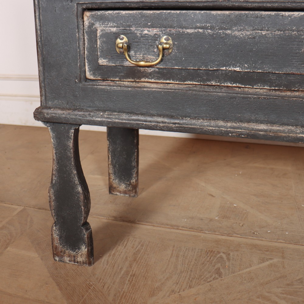 An English painted dresser base featuring a dark charcoal finish, four wide drawers with brass drop handles, shaped corner legs, and a light marble top. View IX