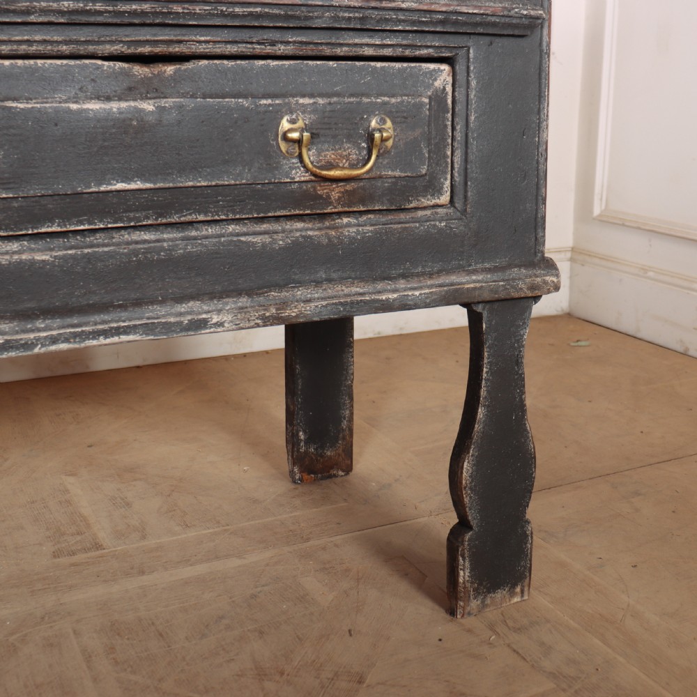An English painted dresser base featuring a dark charcoal finish, four wide drawers with brass drop handles, shaped corner legs, and a light marble top. View X