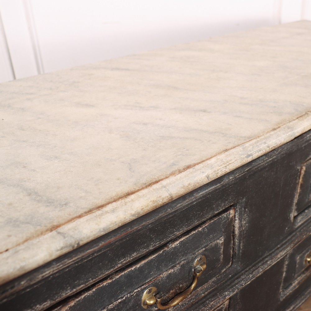 An English painted dresser base featuring a dark charcoal finish, four wide drawers with brass drop handles, shaped corner legs, and a light marble top. View XVI