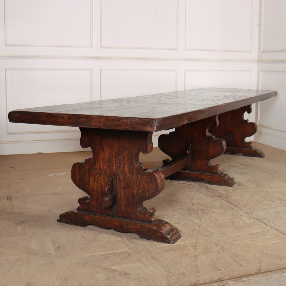 A long antique dark walnut refectory dining table featuring a thick plank top resting on carved trestle supports joined by a central stretcher.