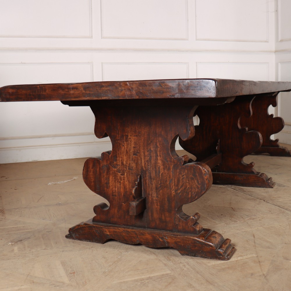 A long antique dark walnut refectory dining table featuring a thick plank top resting on carved trestle supports joined by a central stretcher. View II