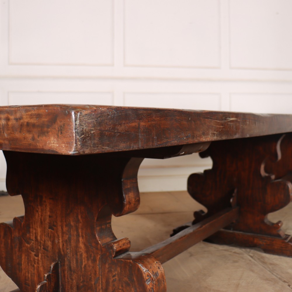 A long antique dark walnut refectory dining table featuring a thick plank top resting on carved trestle supports joined by a central stretcher. View V