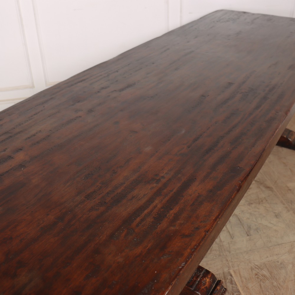 A long antique dark walnut refectory dining table featuring a thick plank top resting on carved trestle supports joined by a central stretcher. View VIII