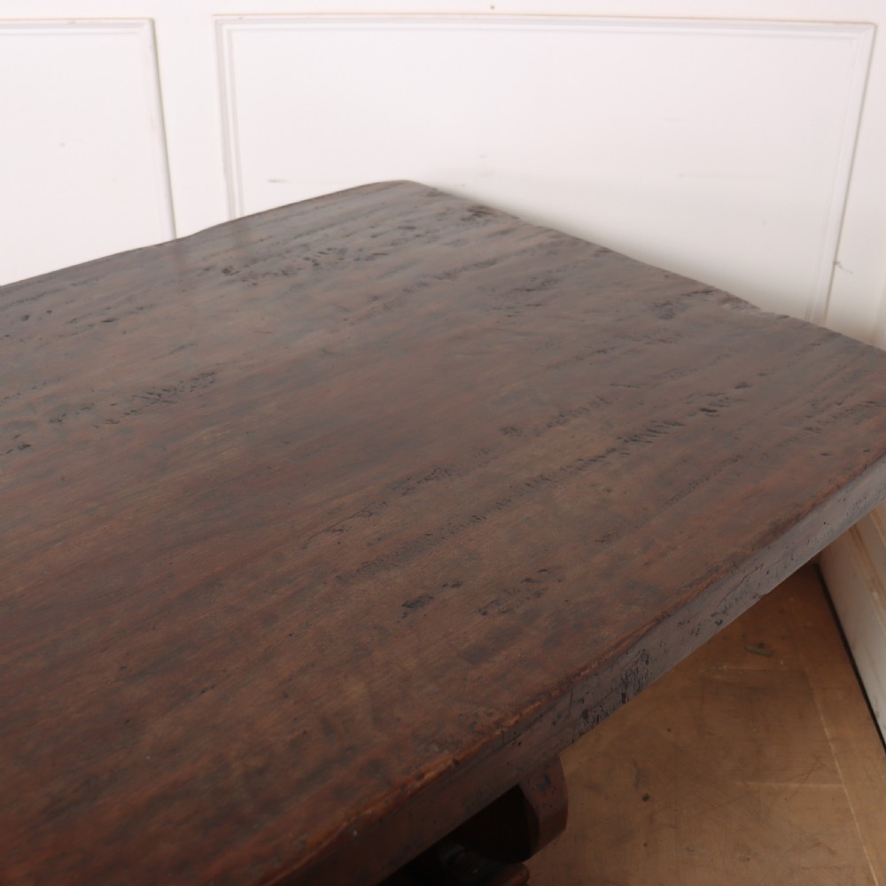 A long antique dark walnut refectory dining table featuring a thick plank top resting on carved trestle supports joined by a central stretcher. View IX