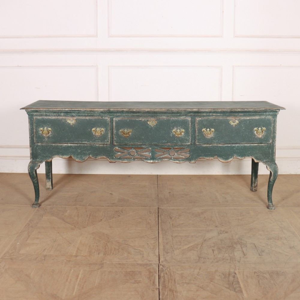 A long antique green painted dresser base featuring three drawers with brass handles, a scalloped apron with pierced fretwork, and cabriole legs.