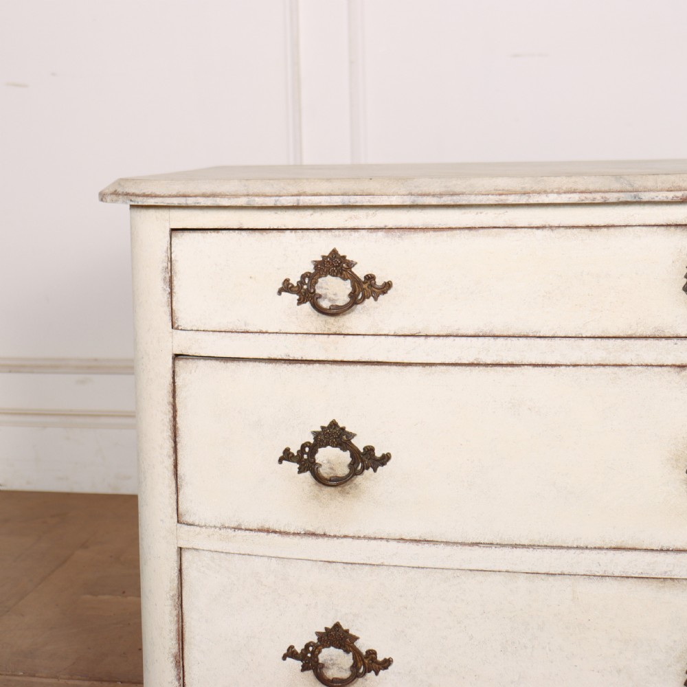 An off-white painted French bow-front commode with three wide drawers, dark metal drop handles, and a light grey marble top. View II