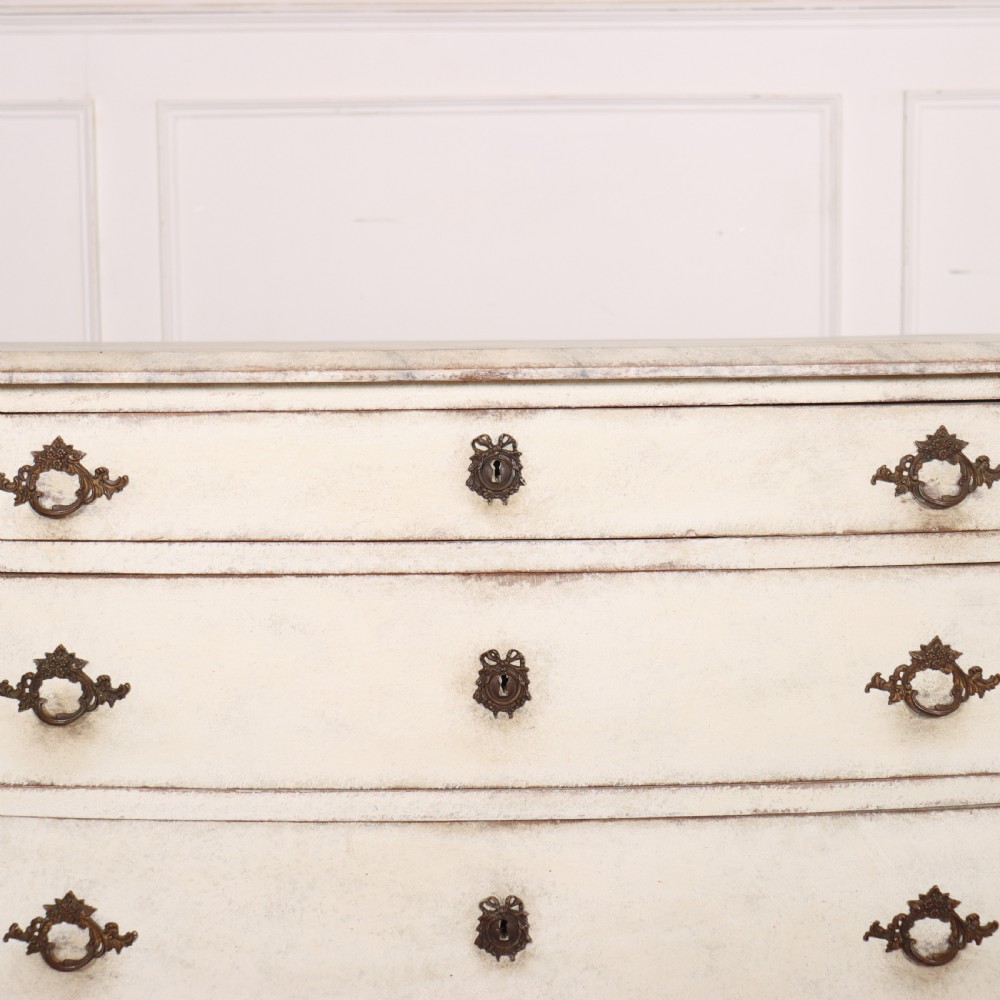 An off-white painted French bow-front commode with three wide drawers, dark metal drop handles, and a light grey marble top. View III