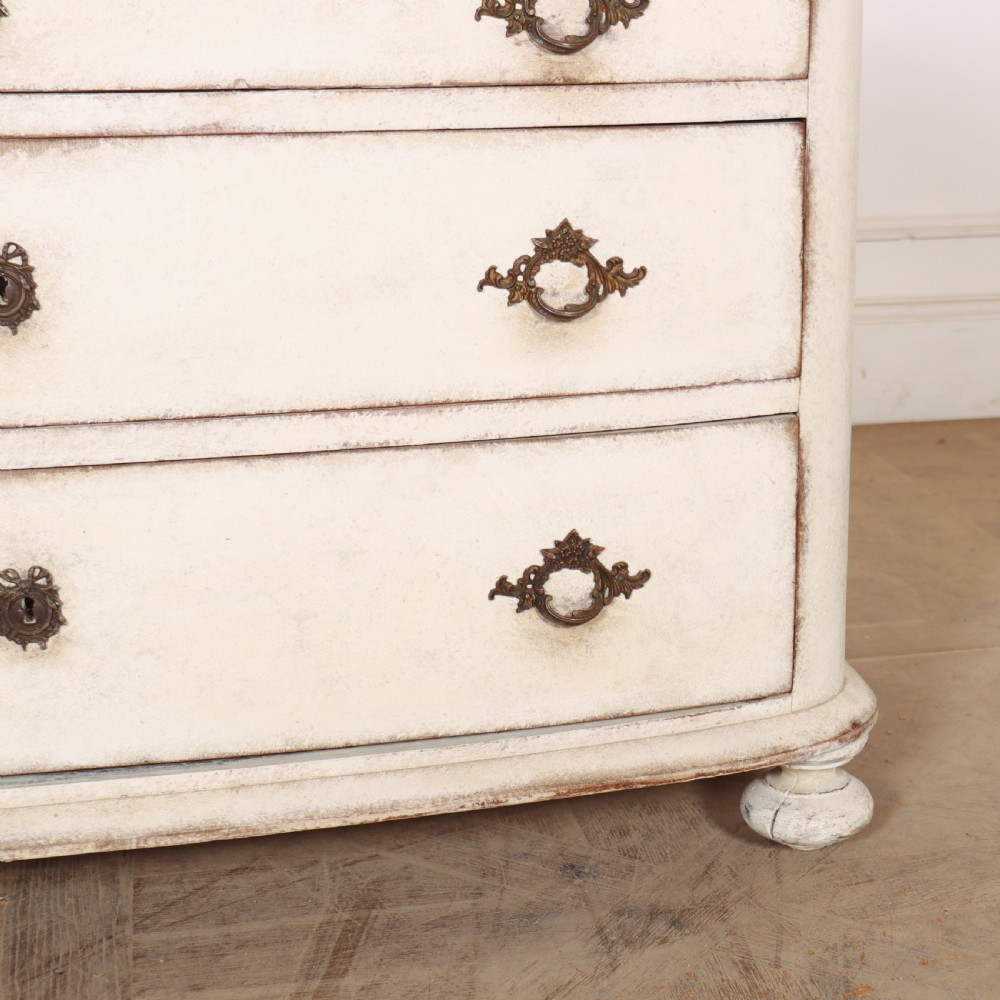 An off-white painted French bow-front commode with three wide drawers, dark metal drop handles, and a light grey marble top. View VI