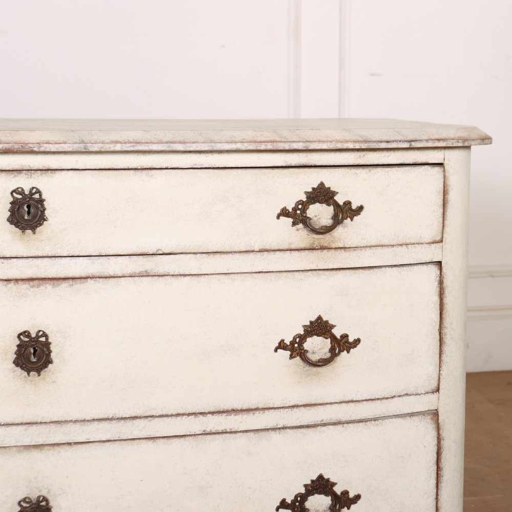 An off-white painted French bow-front commode with three wide drawers, dark metal drop handles, and a light grey marble top. View VII