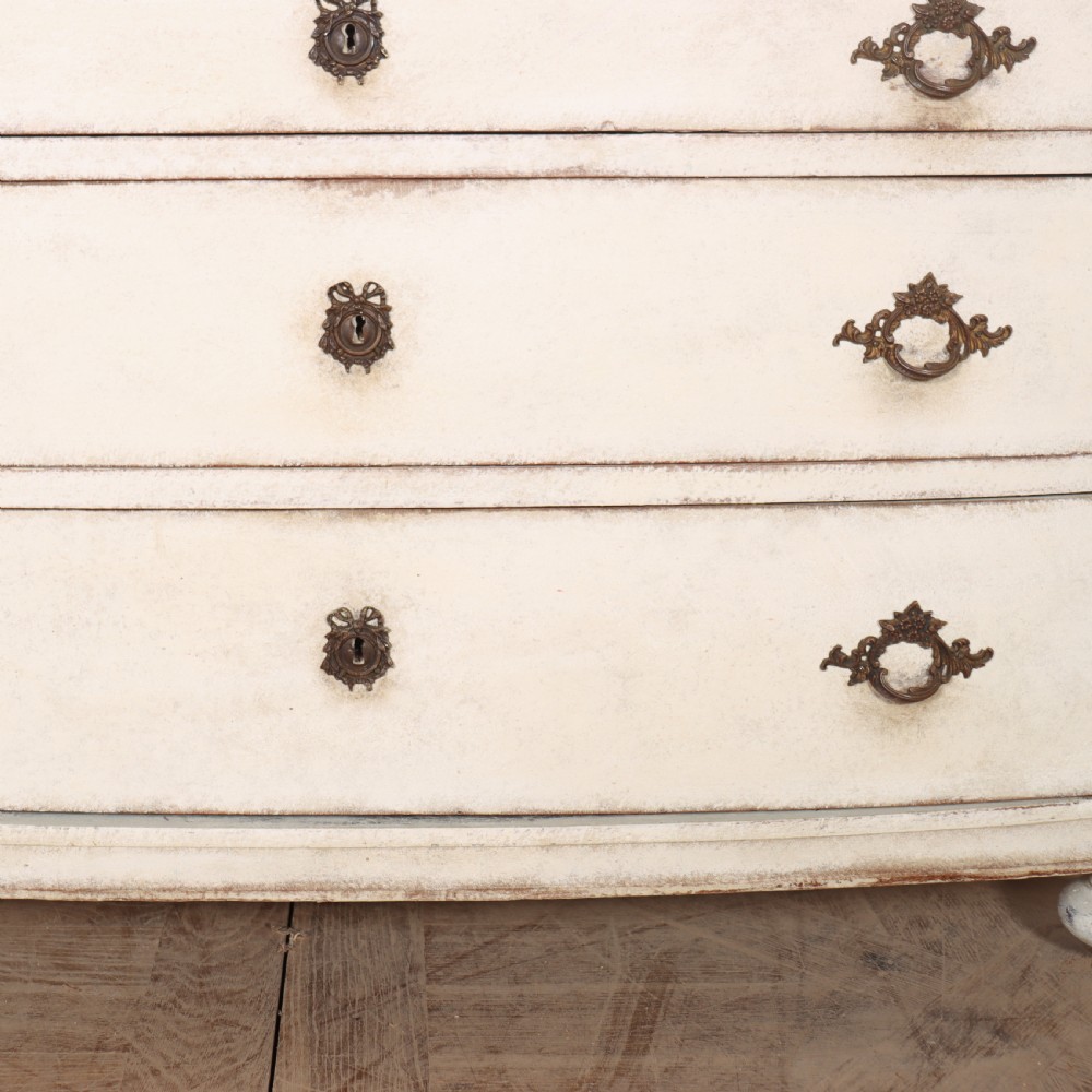 An off-white painted French bow-front commode with three wide drawers, dark metal drop handles, and a light grey marble top. View VIII