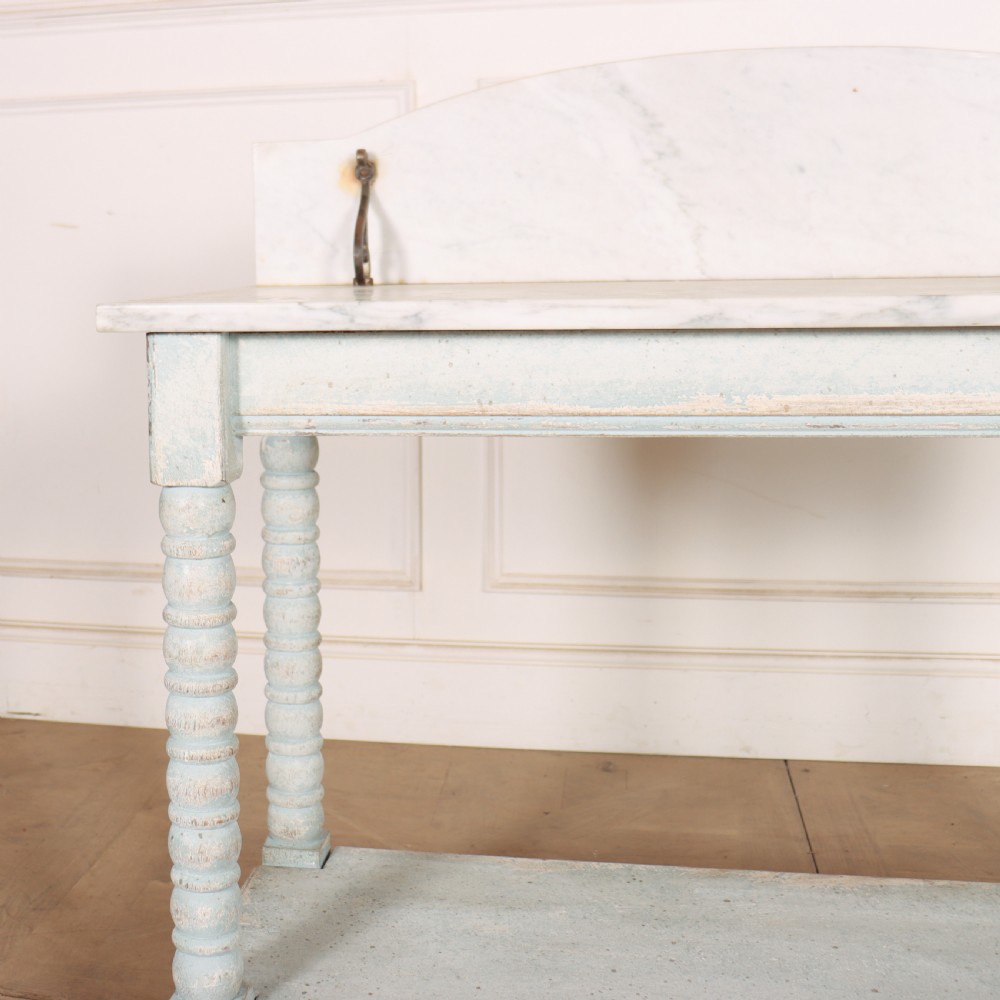 An antique painted wooden washstand featuring bobbin turned legs, a lower shelf, a pale blue distressed finish, and a white marble top with a splashback. View II