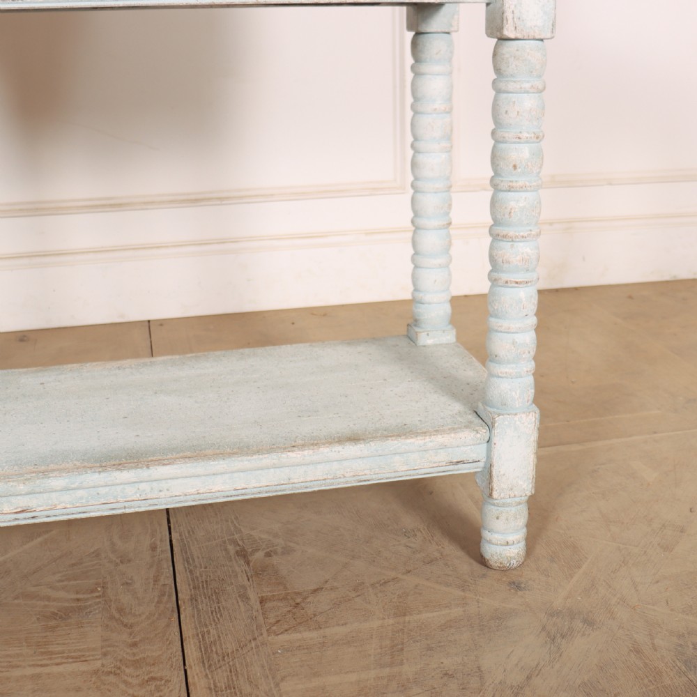An antique painted wooden washstand featuring bobbin turned legs, a lower shelf, a pale blue distressed finish, and a white marble top with a splashback. View IV