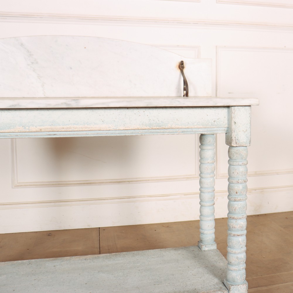 An antique painted wooden washstand featuring bobbin turned legs, a lower shelf, a pale blue distressed finish, and a white marble top with a splashback. View V