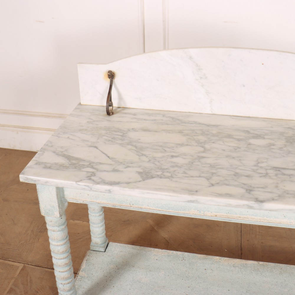 An antique painted wooden washstand featuring bobbin turned legs, a lower shelf, a pale blue distressed finish, and a white marble top with a splashback. View VII