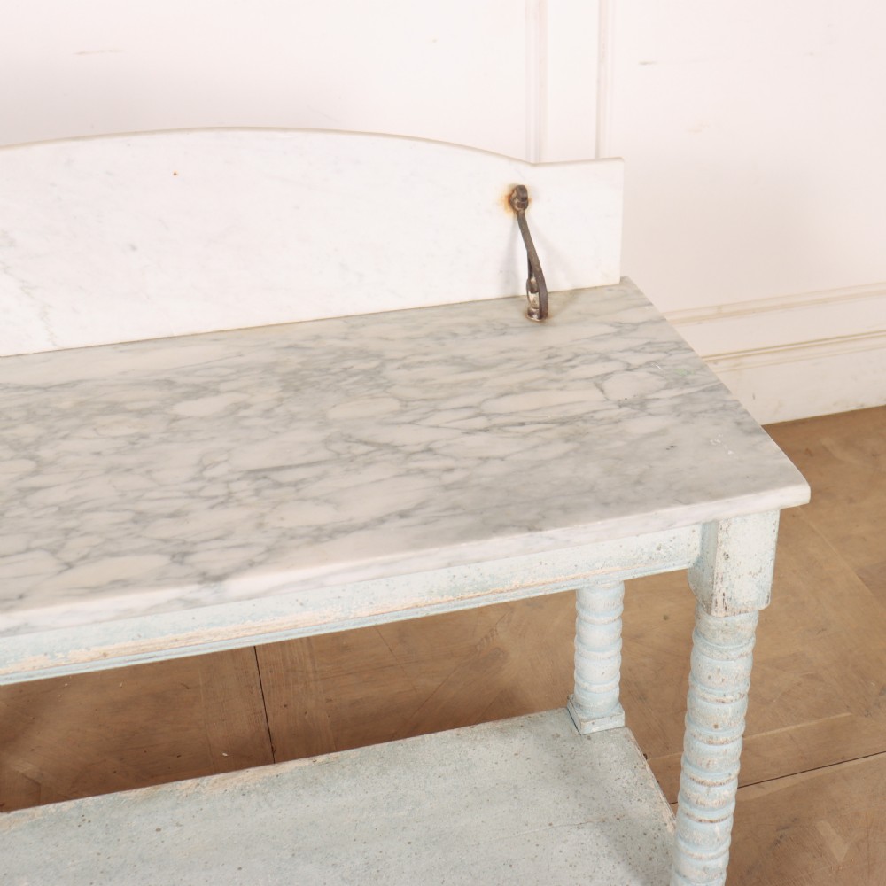 An antique painted wooden washstand featuring bobbin turned legs, a lower shelf, a pale blue distressed finish, and a white marble top with a splashback. View VIII