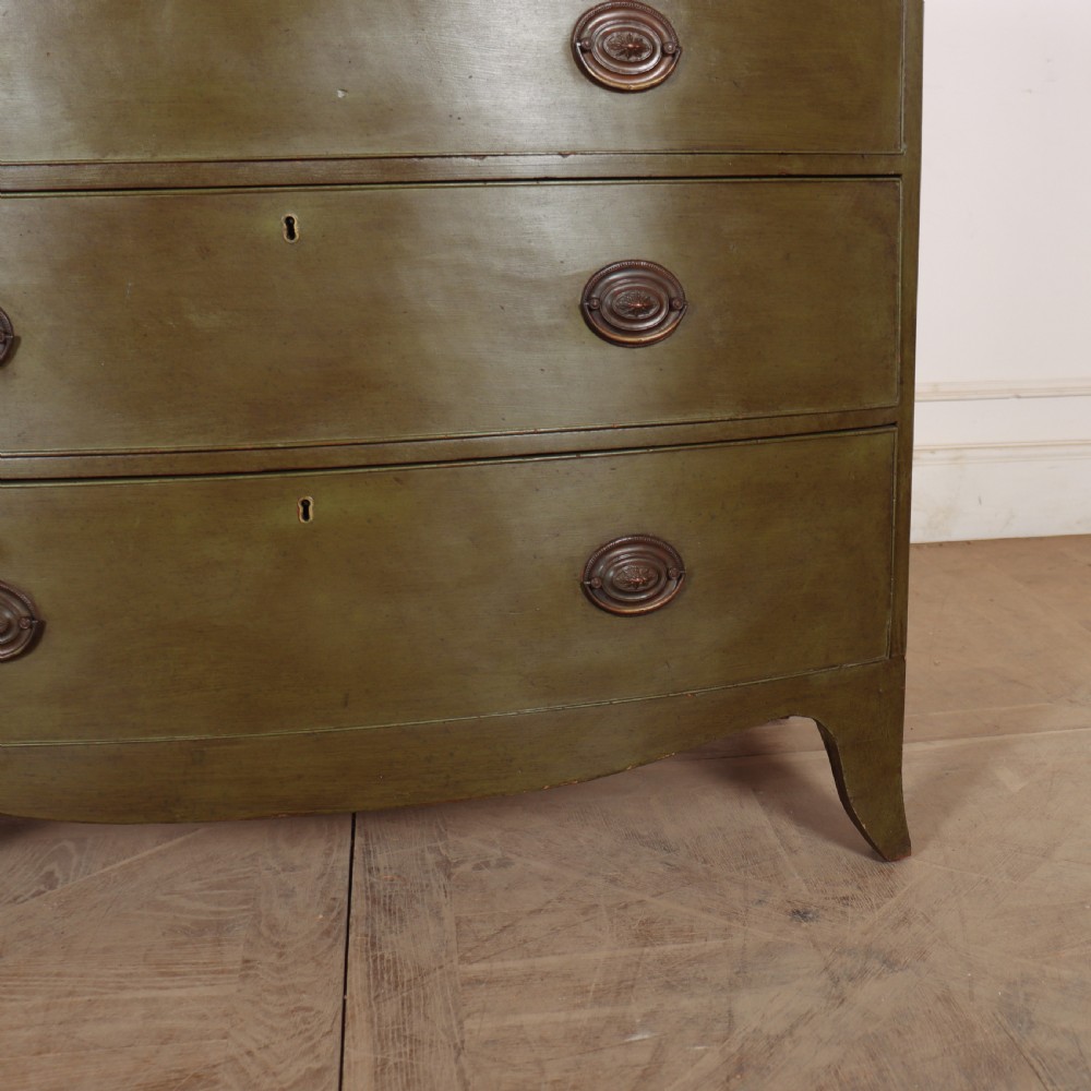 An antique olive green painted bowfront chest of drawers with two short over three long drawers and oval brass handles. View VII