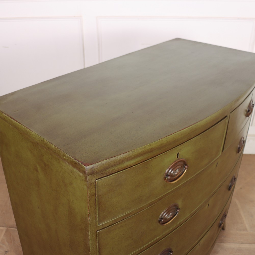 An antique olive green painted bowfront chest of drawers with two short over three long drawers and oval brass handles. View IX