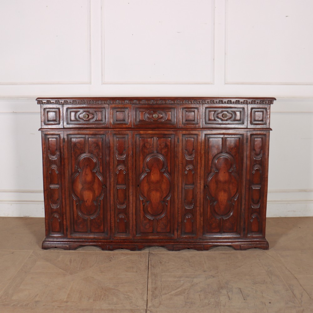 An antique dark walnut Italian sideboard featuring three upper frieze drawers and three carved panelled doors.