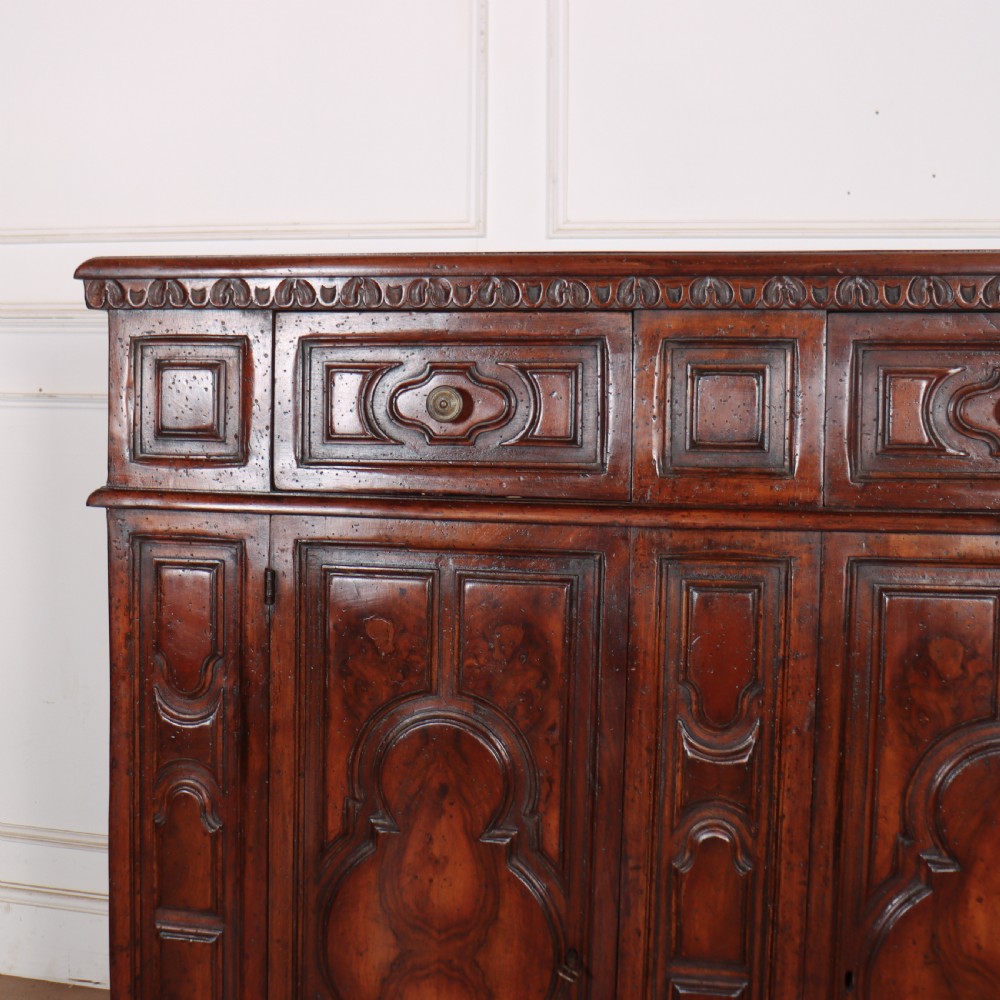 An antique dark walnut Italian sideboard featuring three upper frieze drawers and three carved panelled doors. View II