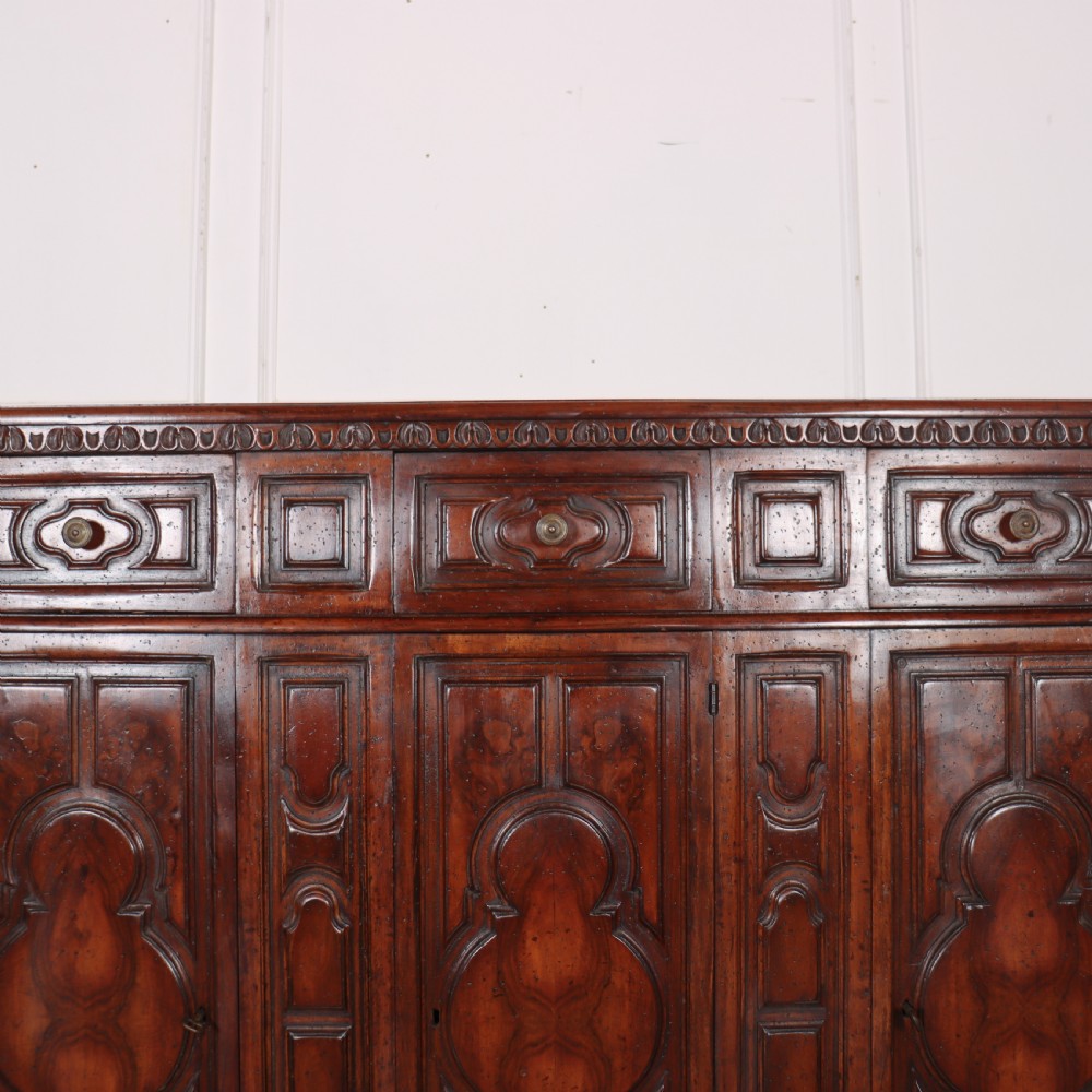 An antique dark walnut Italian sideboard featuring three upper frieze drawers and three carved panelled doors. View V