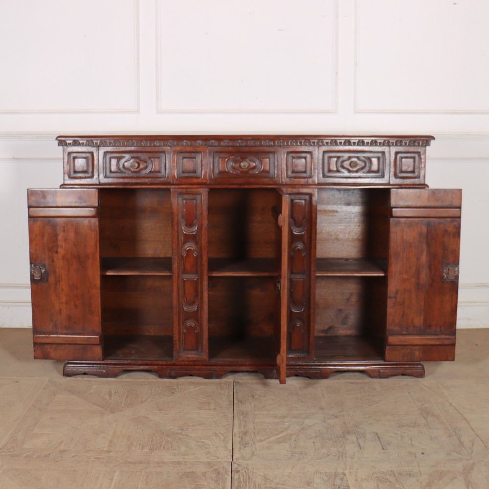 An antique dark walnut Italian sideboard featuring three upper frieze drawers and three carved panelled doors. View X