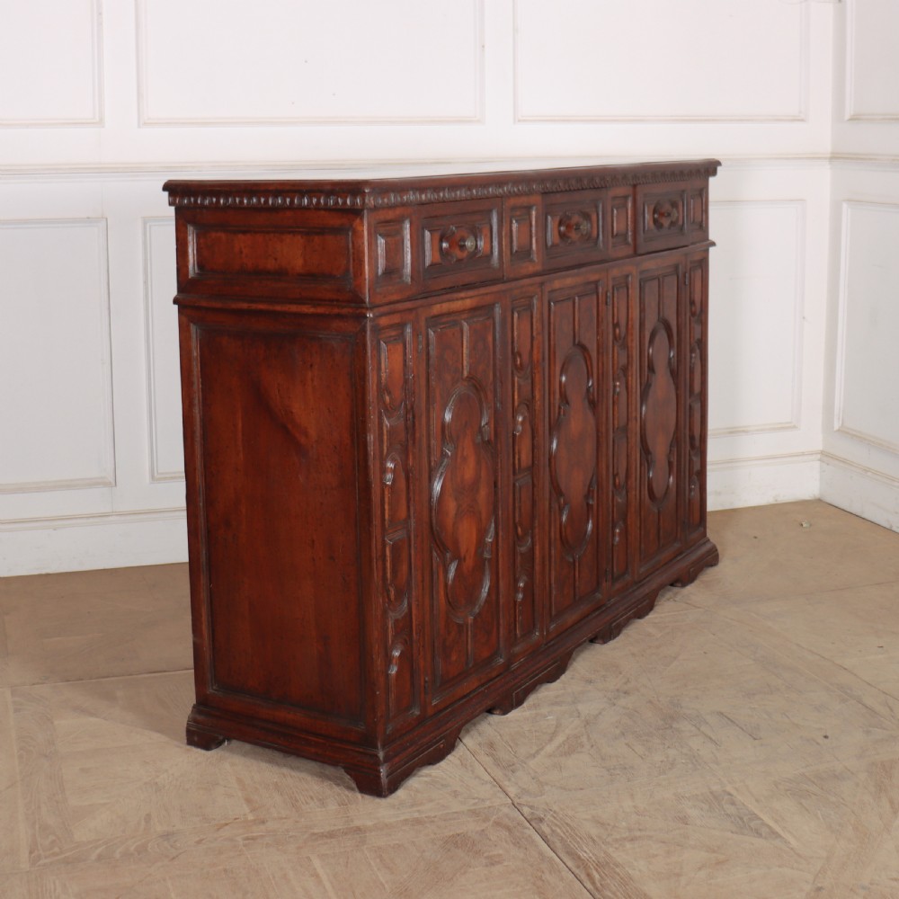 An antique dark walnut Italian sideboard featuring three upper frieze drawers and three carved panelled doors. View XI