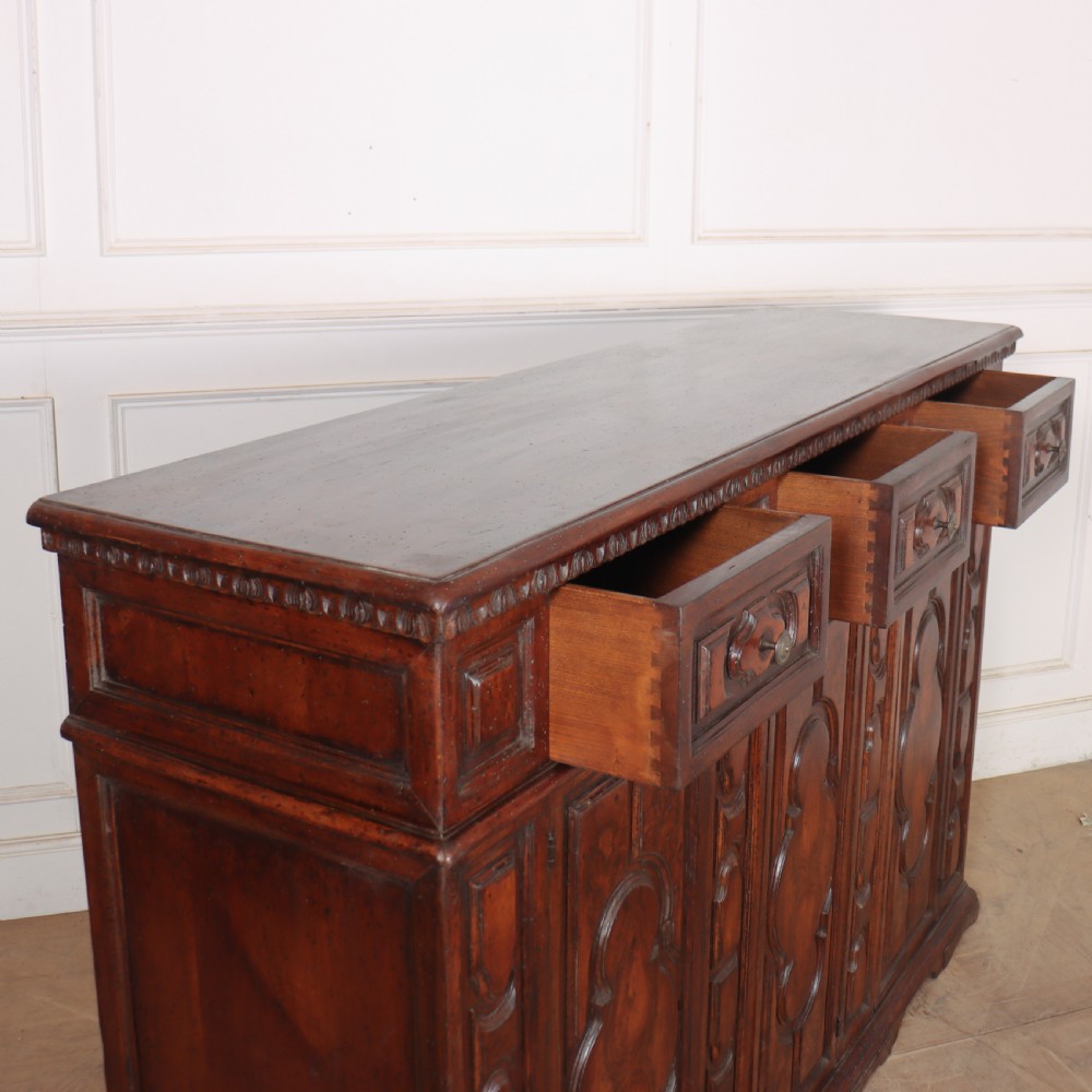 An antique dark walnut Italian sideboard featuring three upper frieze drawers and three carved panelled doors. View XIV