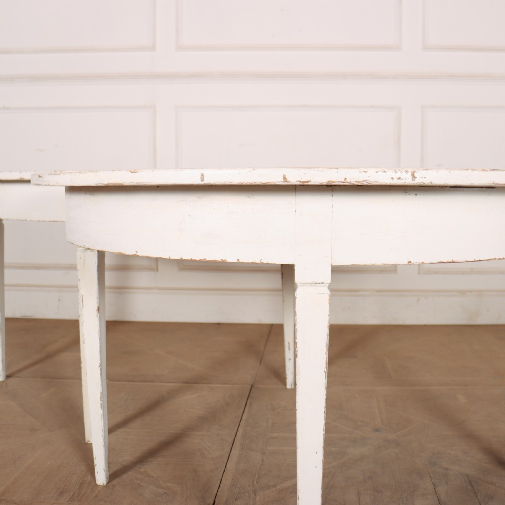 A pair of Swedish demi-lune console tables featuring a distressed off-white painted finish and slender tapered legs. View II