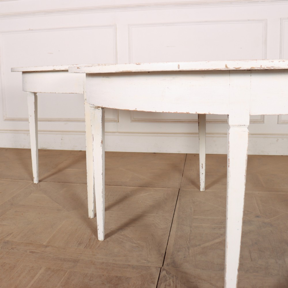 A pair of Swedish demi-lune console tables featuring a distressed off-white painted finish and slender tapered legs. View III