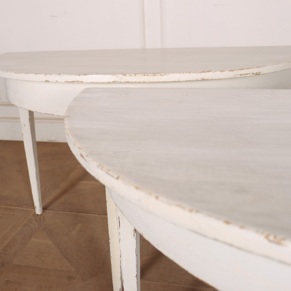 A pair of Swedish demi-lune console tables featuring a distressed off-white painted finish and slender tapered legs. View IV