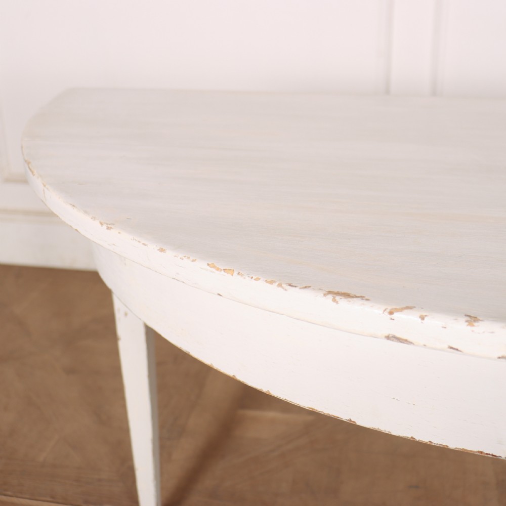 A pair of Swedish demi-lune console tables featuring a distressed off-white painted finish and slender tapered legs. View VI