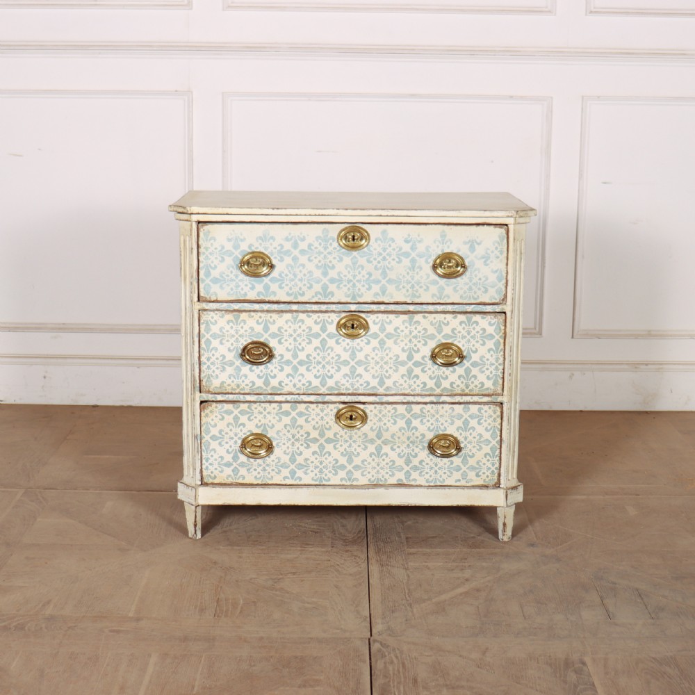 A Swedish painted oak commode featuring three drawers with light blue stencilled motifs, brass ring handles, and fluted corner pilasters.