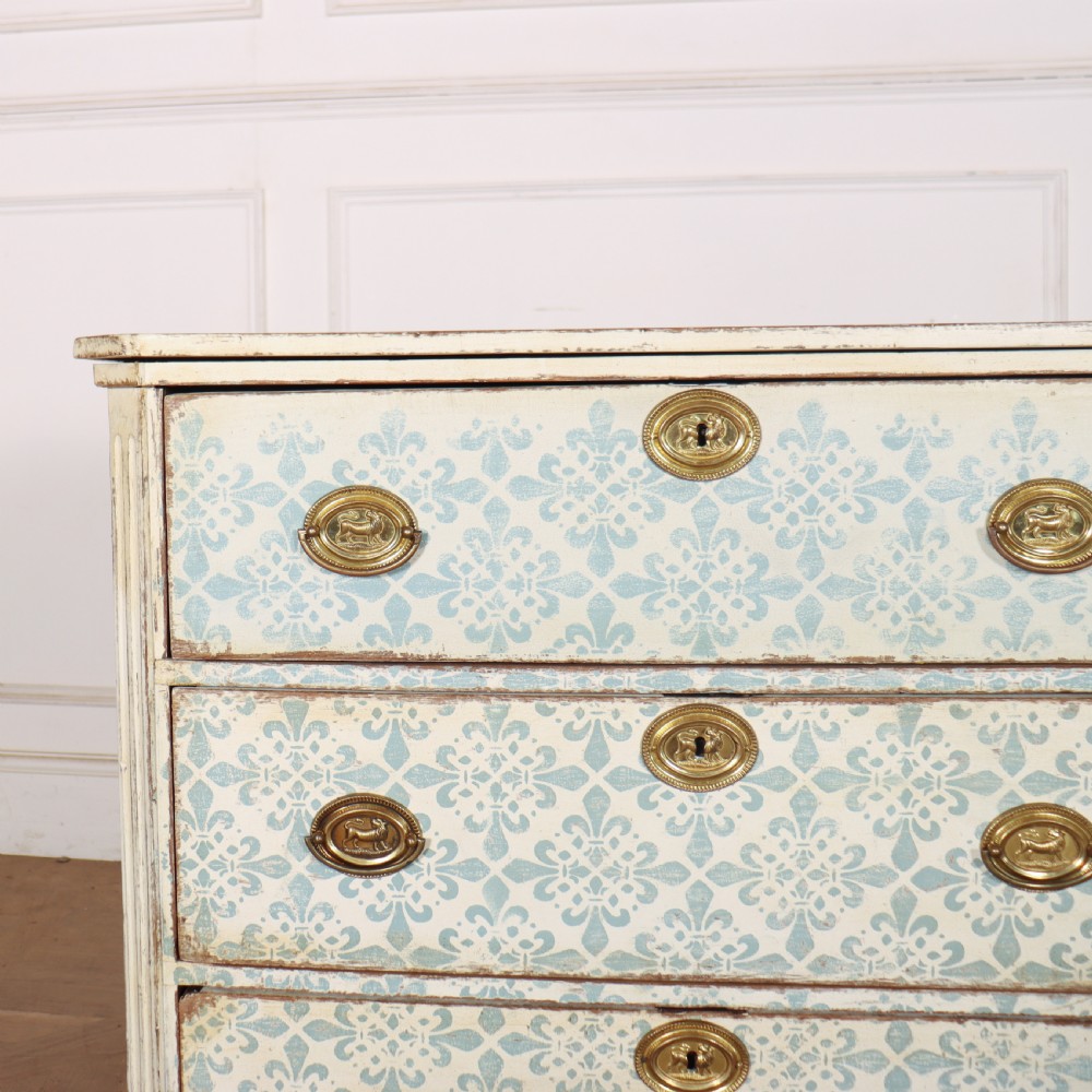 A Swedish painted oak commode featuring three drawers with light blue stencilled motifs, brass ring handles, and fluted corner pilasters. View II
