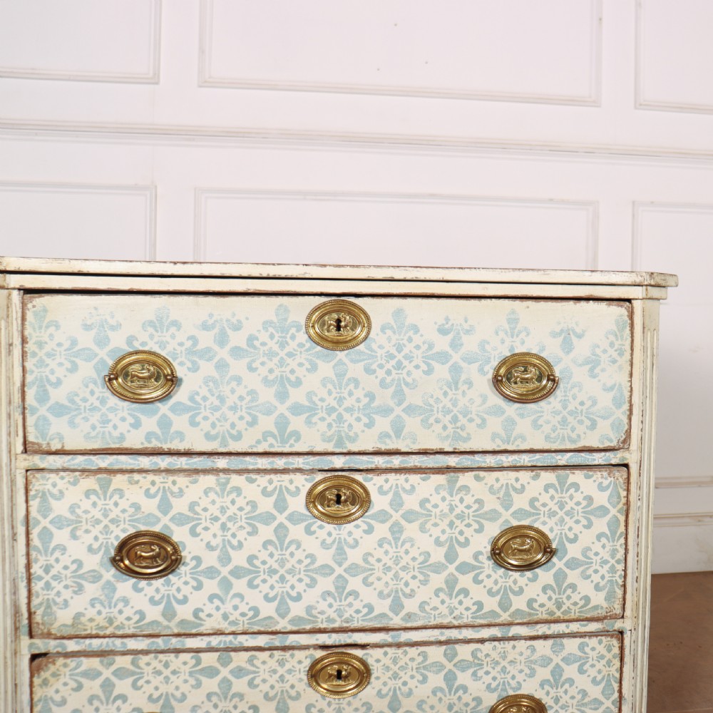 A Swedish painted oak commode featuring three drawers with light blue stencilled motifs, brass ring handles, and fluted corner pilasters. View III