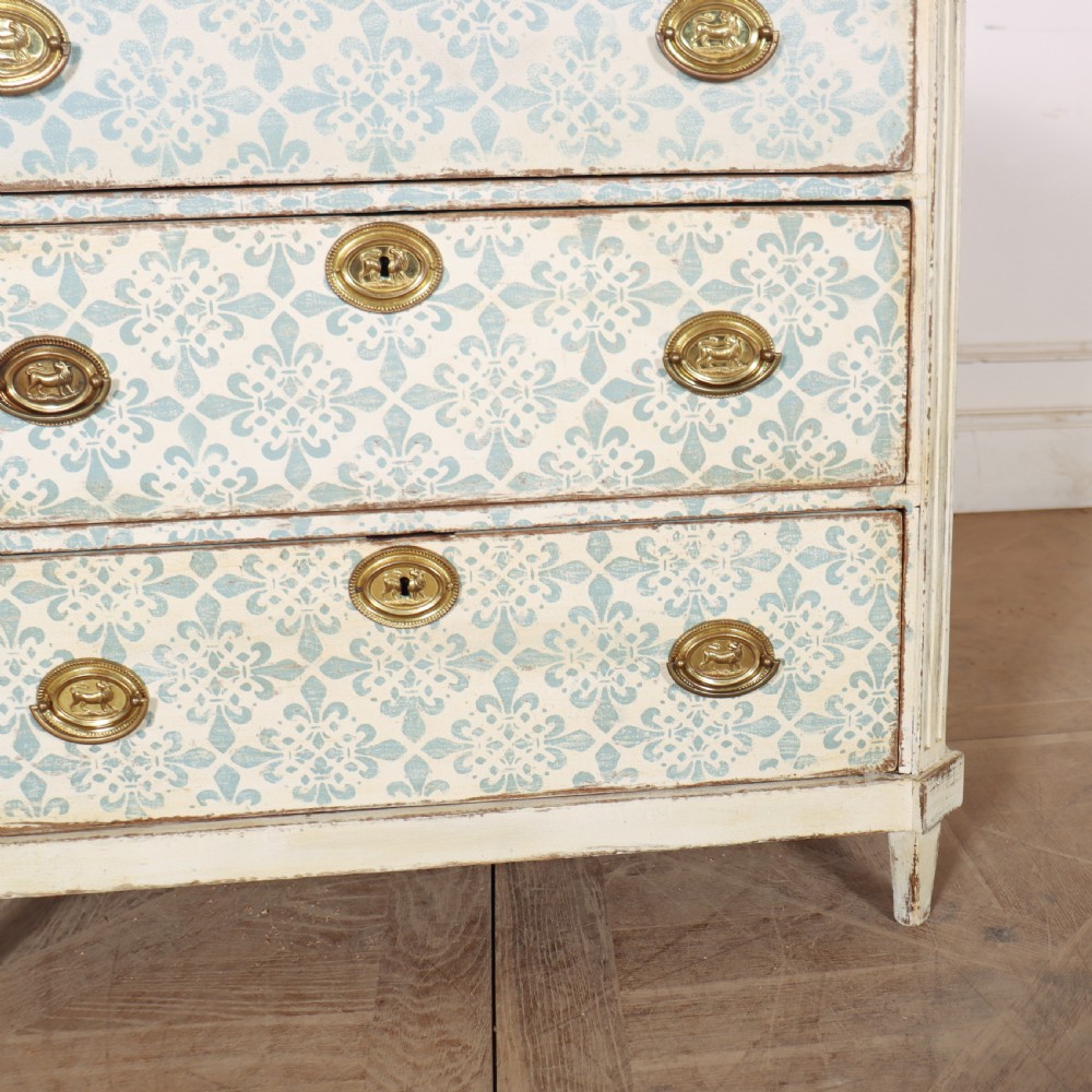 A Swedish painted oak commode featuring three drawers with light blue stencilled motifs, brass ring handles, and fluted corner pilasters. View IV