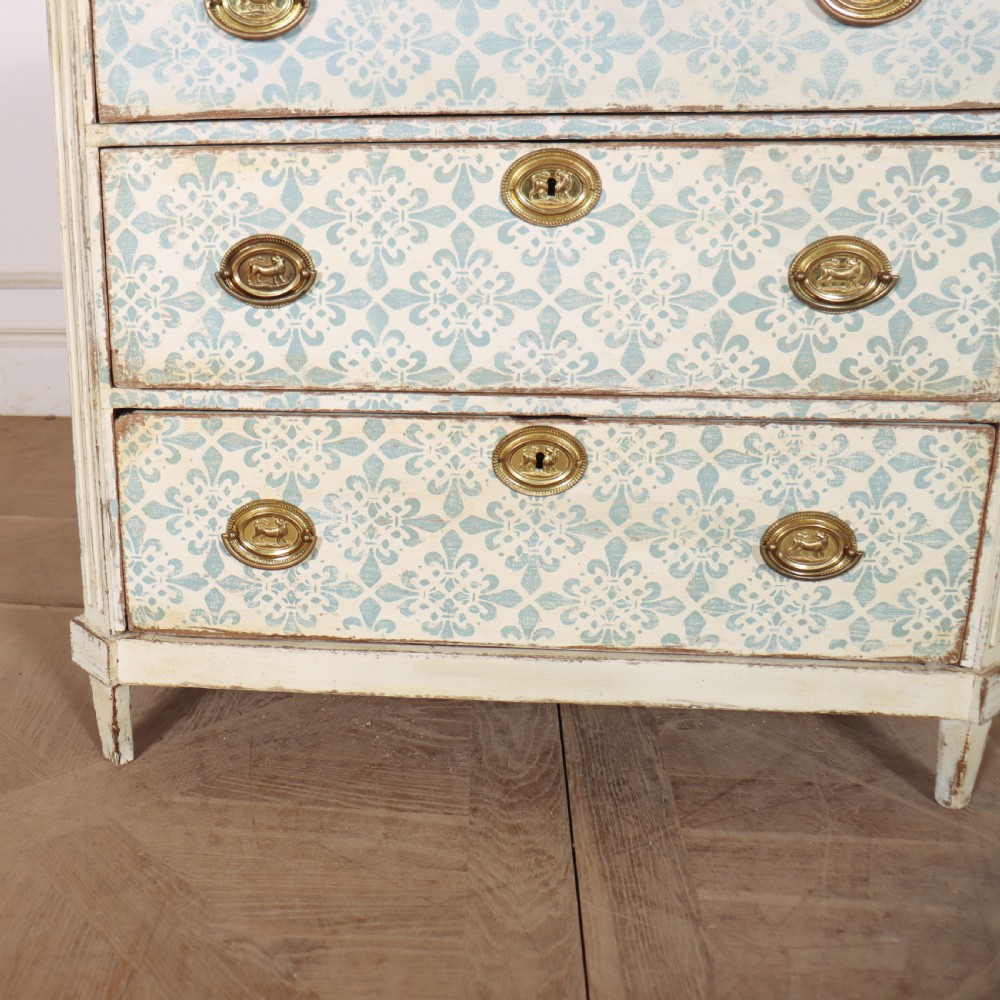 A Swedish painted oak commode featuring three drawers with light blue stencilled motifs, brass ring handles, and fluted corner pilasters. View V