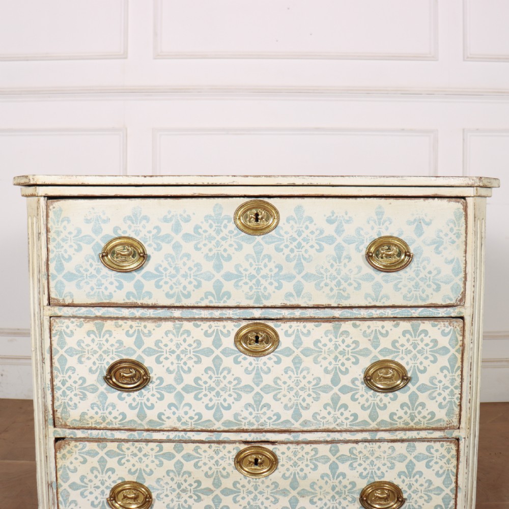 A Swedish painted oak commode featuring three drawers with light blue stencilled motifs, brass ring handles, and fluted corner pilasters. View VI