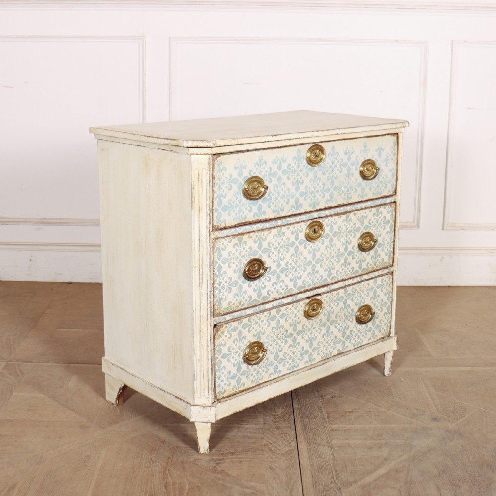 A Swedish painted oak commode featuring three drawers with light blue stencilled motifs, brass ring handles, and fluted corner pilasters. View VII