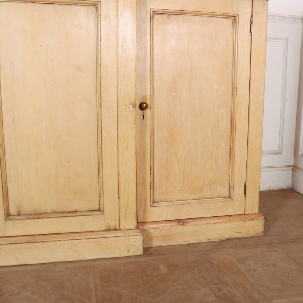A wide English pine breakfront cupboard featuring four recessed panel doors, brass knobs, and a projecting central section. View IV
