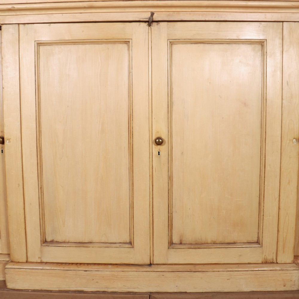 A wide English pine breakfront cupboard featuring four recessed panel doors, brass knobs, and a projecting central section. View V