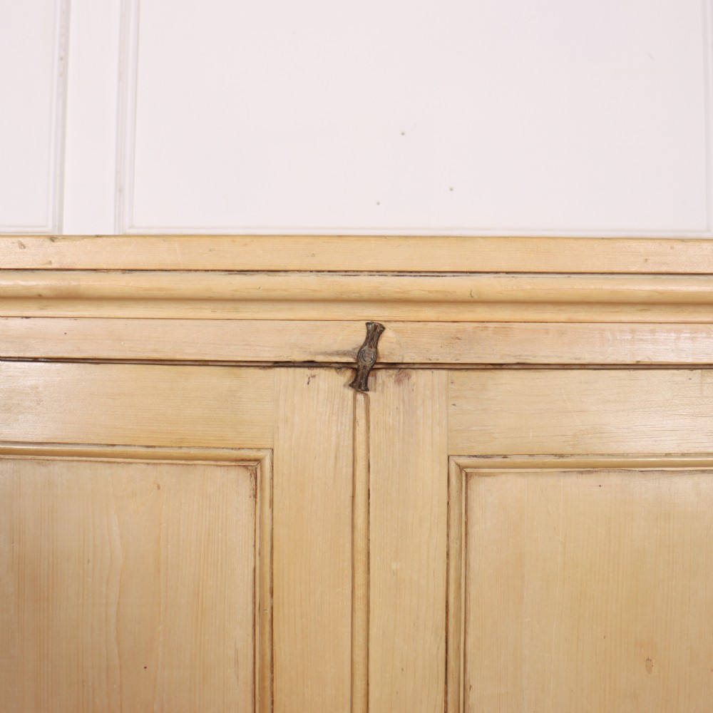 A wide English pine breakfront cupboard featuring four recessed panel doors, brass knobs, and a projecting central section. View VII