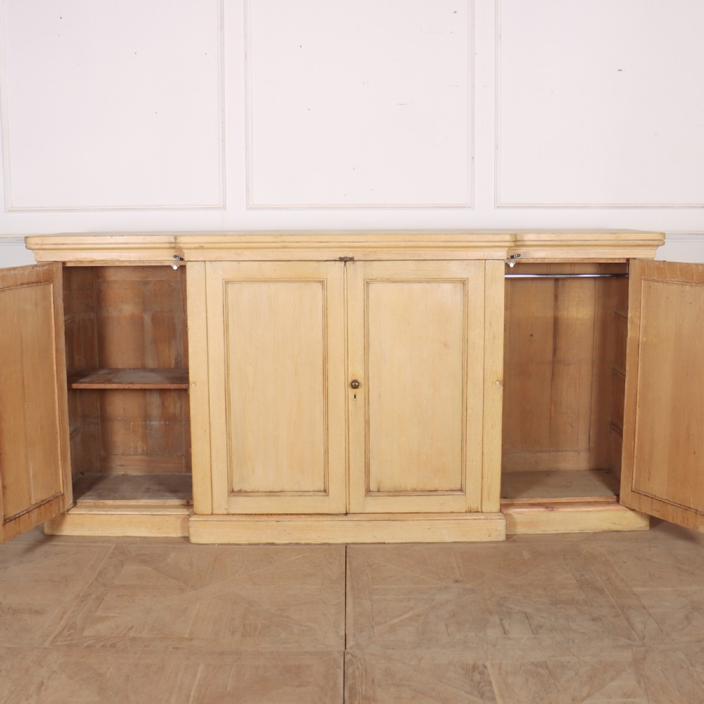 A wide English pine breakfront cupboard featuring four recessed panel doors, brass knobs, and a projecting central section. View VIII