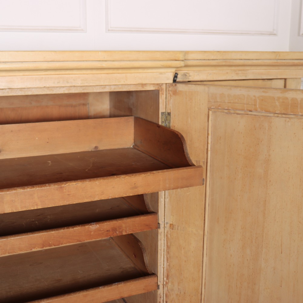 A wide English pine breakfront cupboard featuring four recessed panel doors, brass knobs, and a projecting central section. View XI