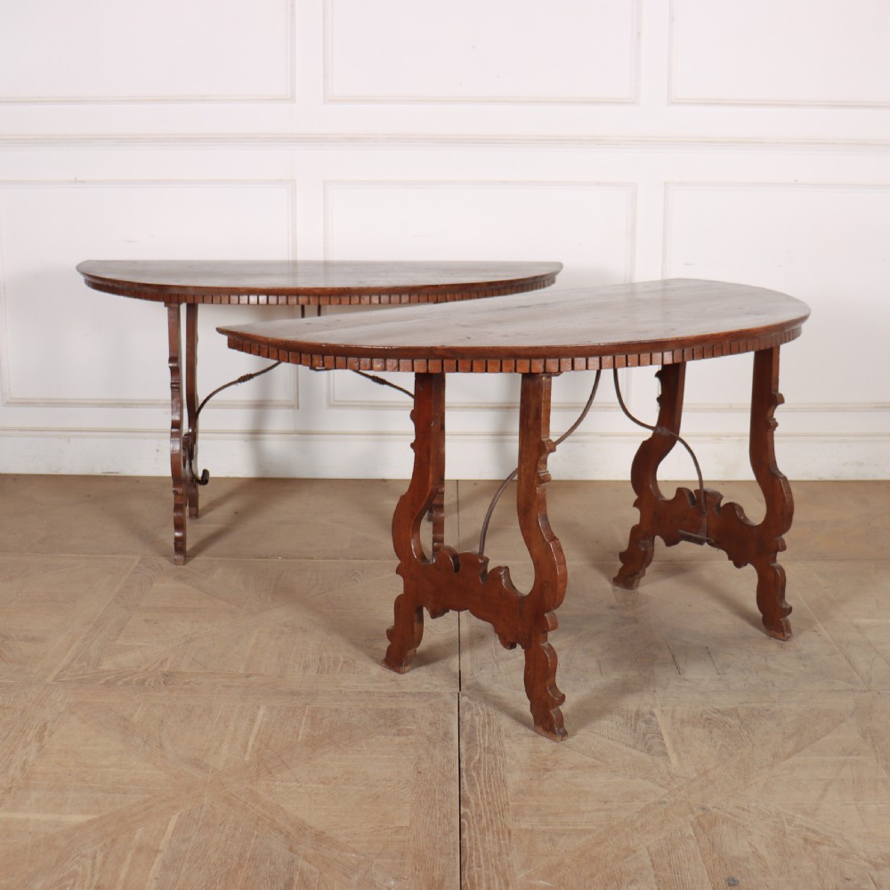 A pair of semi-circular Italian walnut console tables with carved apron detailing, lyre-shaped legs, and curved wrought iron stretchers.