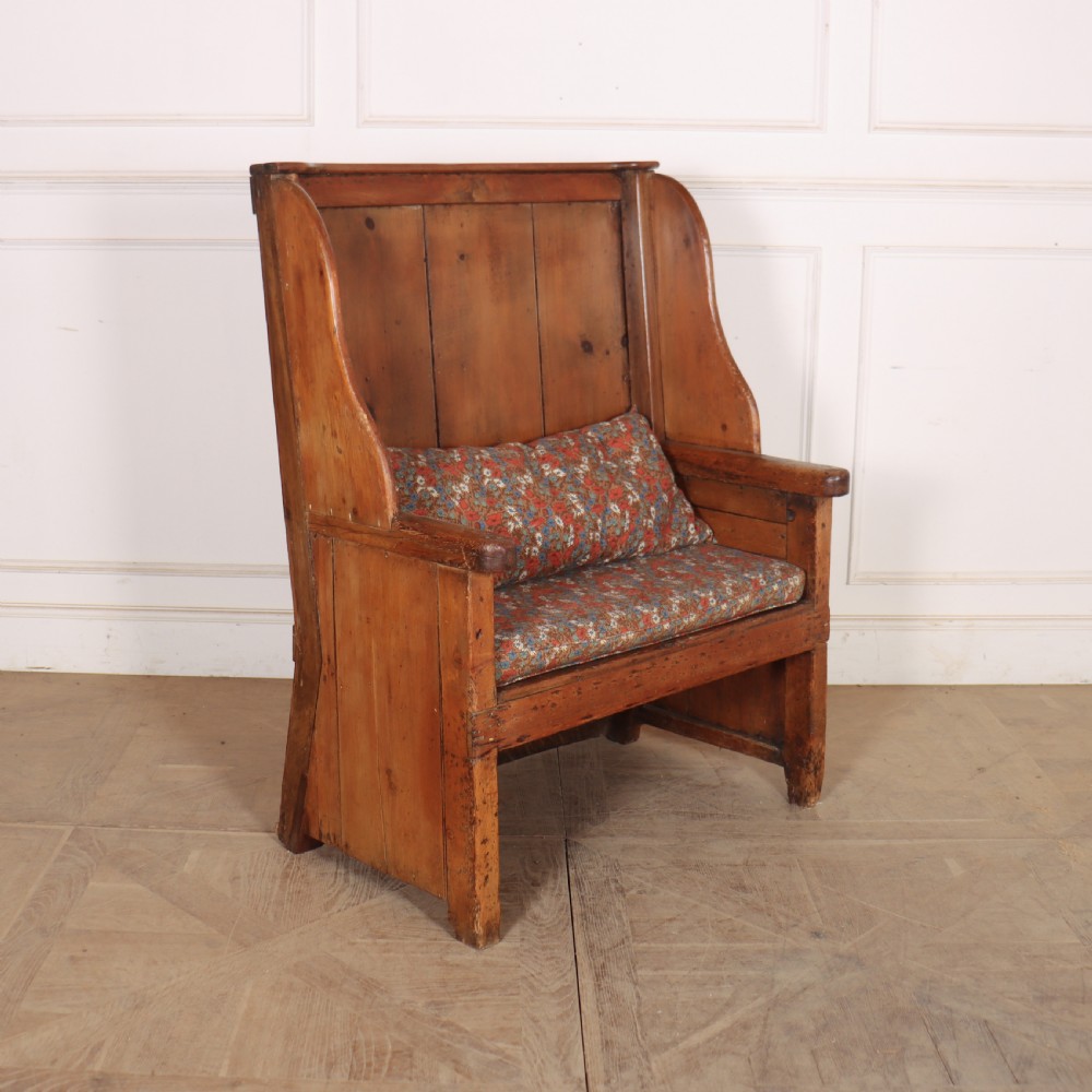 A high-backed antique pine wooden settle featuring tall vertical plank panels, curved side wings, and a floral upholstered seat cushion. View II