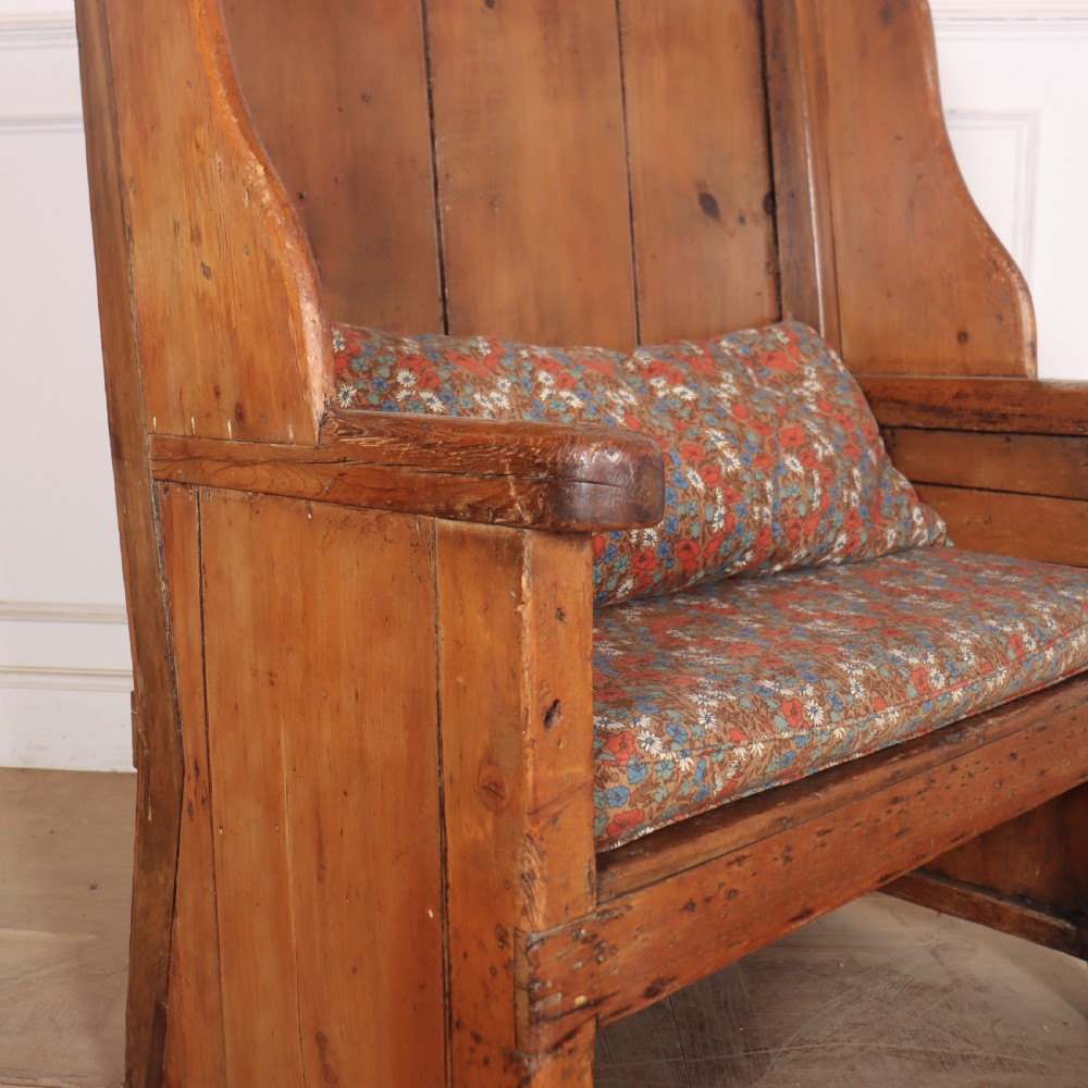 A high-backed antique pine wooden settle featuring tall vertical plank panels, curved side wings, and a floral upholstered seat cushion. View IV