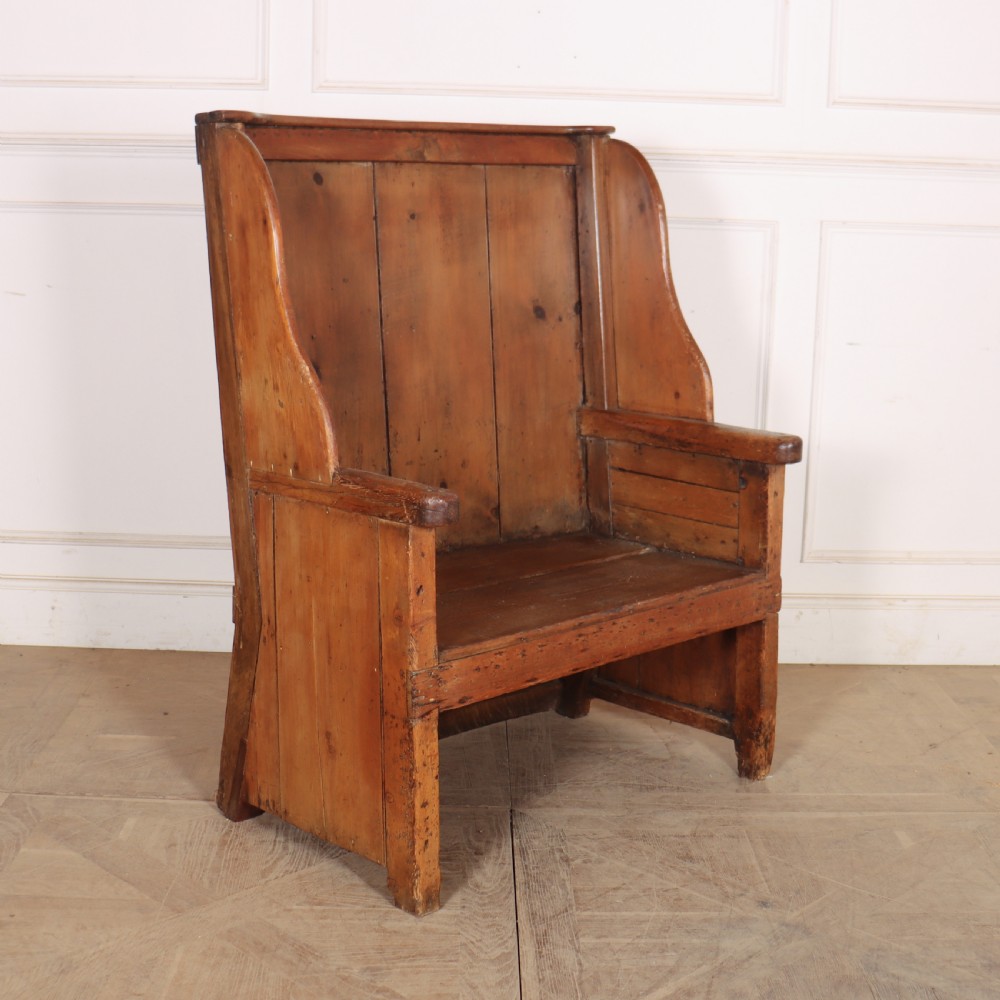 A high-backed antique pine wooden settle featuring tall vertical plank panels, curved side wings, and a floral upholstered seat cushion. View V
