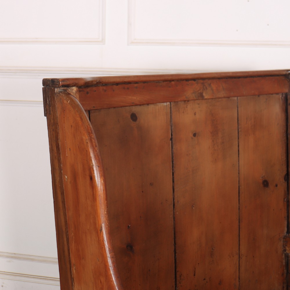 A high-backed antique pine wooden settle featuring tall vertical plank panels, curved side wings, and a floral upholstered seat cushion. View VI